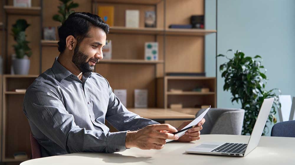 business man employee working on laptop looking at document at home office.