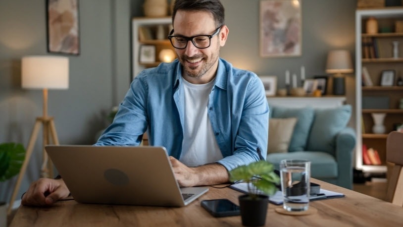 Man sitting at desk, looking at laptop.